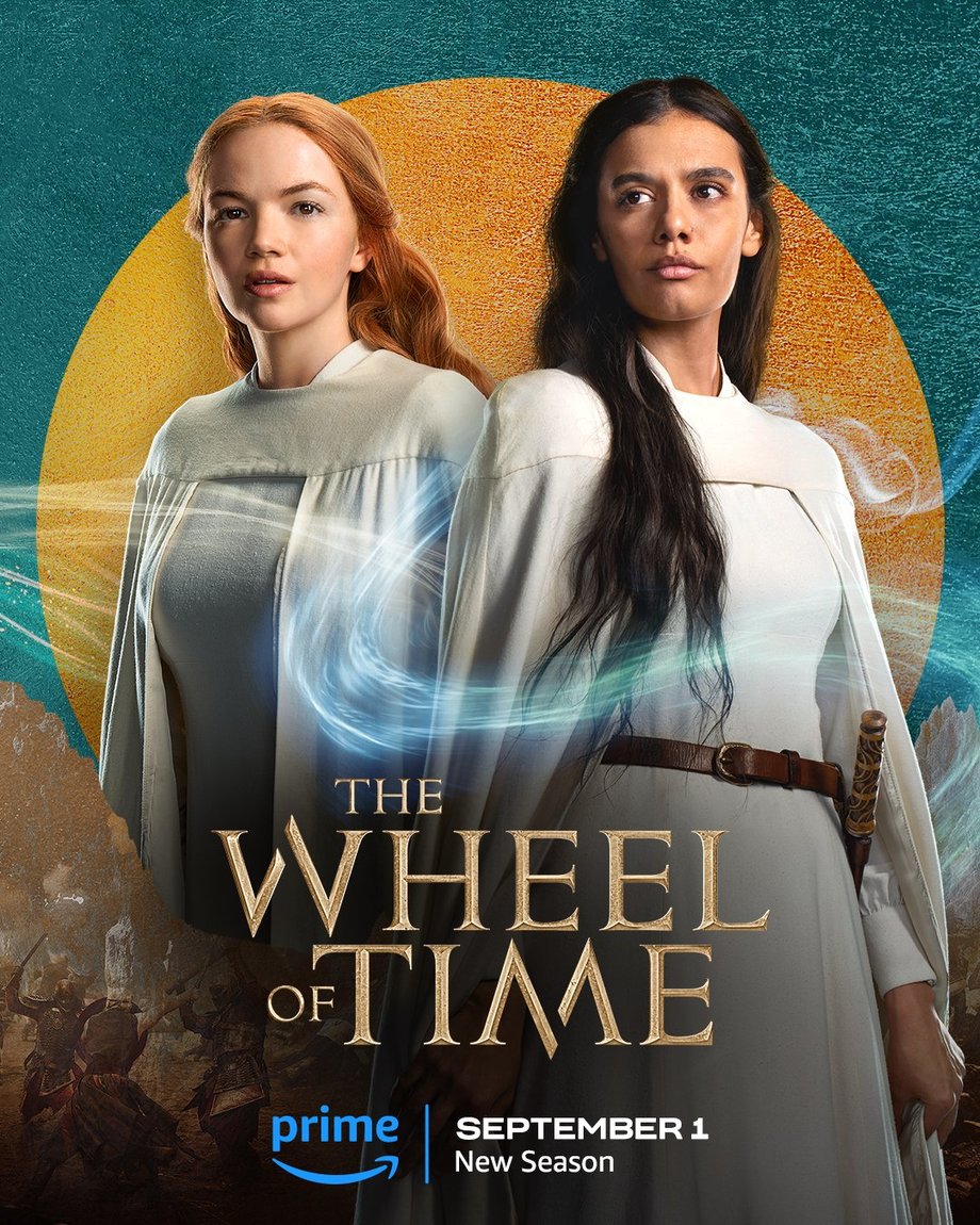 A large gold leaf-textured circle sits atop a teal foil background. The jutting peaks of mountains are beneath the circle, with people locked in battle in front of the range. Two characters are featured centered in the image. In the foreground on the right, Egwene is featured in a medium shot. Her long dark hair hangs loose over her shoulders; she wears a white cloak over a dress of the same color; and an illuminated weave wraps across her torso and over right shoulder. Behind her to the left stands Elayne, also shown in a medium shot. Her hair is worn half-up; she wears a white cloak over a dress of the same color; and illuminated weaves wrap around her body as she stares off in the distance. Golden text in the lower center reads, “The Wheel of Time.” At the bottom, the blue Prime Video logo sits next to white text that says “September 1, New Season.”