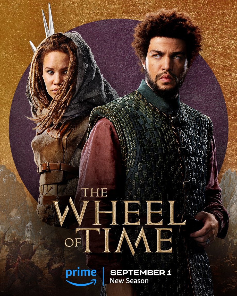 A large purple foil circle sits atop a gold leaf-textured background. The jutting peaks of mountains are beneath the circle, with people locked in battle in front of the range. Two characters are featured centered in the image. In the foreground on the right, Perrin is featured in a medium shot. He wears a patterned vest over a purple long-sleeve shirt. Behind him to the left stands Aviendha, also shown in a medium shot. She wears a protective leather vest, a veil over her long hair, and spears peek from behind her shoulder. Golden text in the lower center reads, “The Wheel of Time.” At the bottom, the blue Prime Video logo sits next to white text that says “September 1, New Season.”
